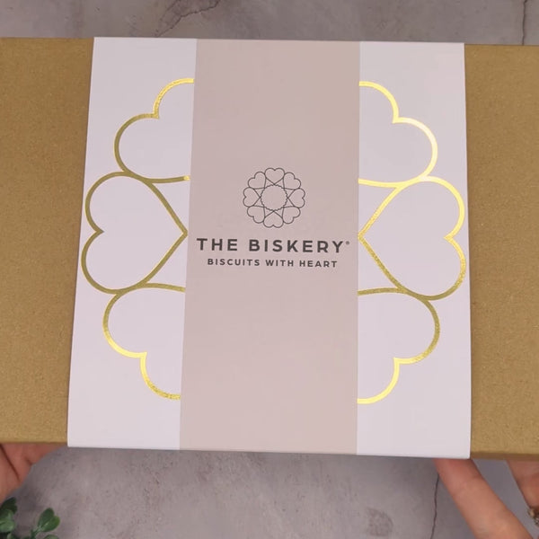A person turns around a box labelled "The Biskery" and "Love Every Bite." Inside the box are "50th birthday" biscuits