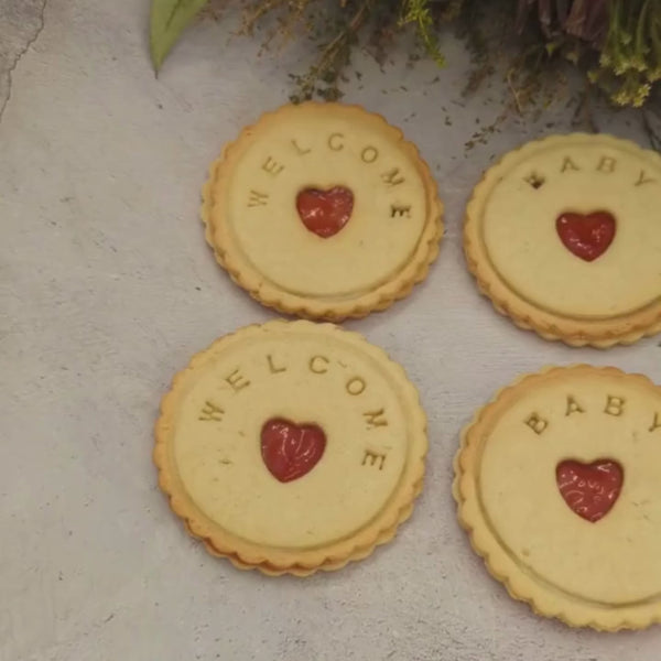 Close-up view of branded jam biscuits from The Biskery company with 'WELCOME', 'BABY', and a personalised name messages