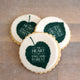 Image of three cookies sitting on top of each other. The cookies are on a white background. The cookies are a light brown color and have the words "THE HEART OF ENGLAND FOREST" printed on them in white letters. There is a small green leaf on top of all the cookies. Biscuits are made by The Biskery