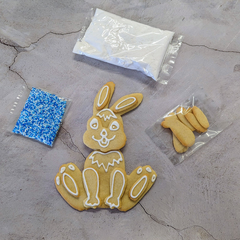 Cookie DIY Kit: White bunny-shaped cookie with white icing, next to sprinkles and sugar.