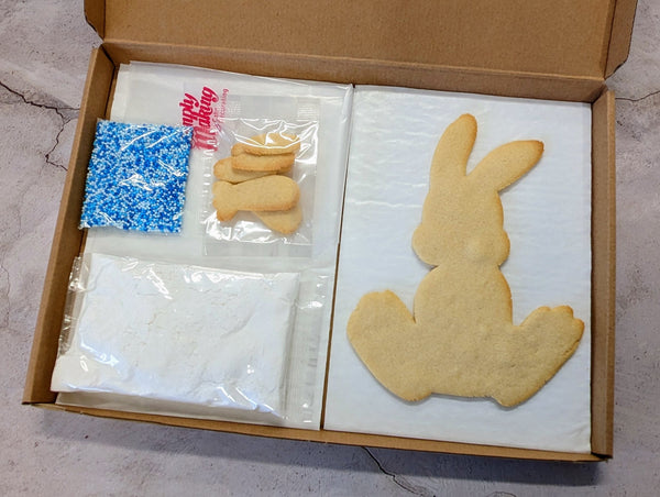 Cookie DIY Kit from The Biskery in the box bunny-shaped cookie with white icing, next to sprinkles and sugar.