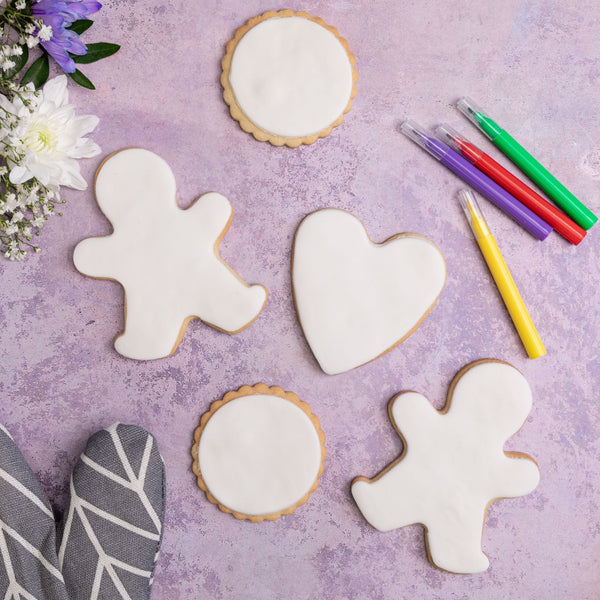 A variety of plain iced biscuits on a purple background. The biscuits include a gingerbread man, heart, and circle biscuits, all decorated with white fondant.