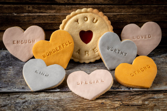 Iced Affirmation biscuits on display. A variety of heart-shaped biscuits decorated with the words 'LOVED', 'WONDERFUL', 'WORTHY', 'ENOUGH', 'STRONG', 'KIND', and 'SPECIAL'
