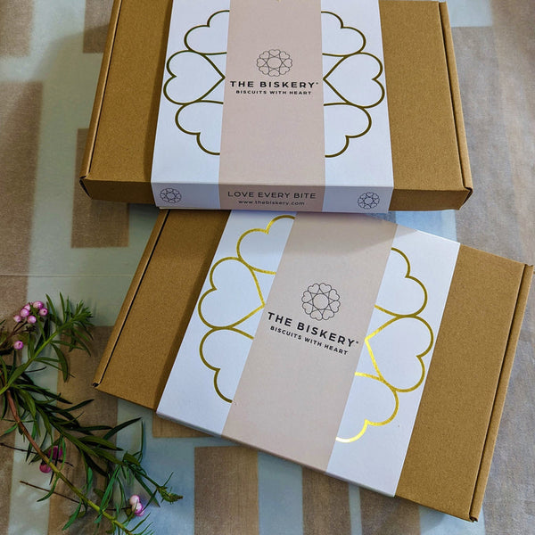  Boxes labelled 'The Biskery' and 'Love Every Bite' sitting on a table, filled with Valentine's Day biscuits.