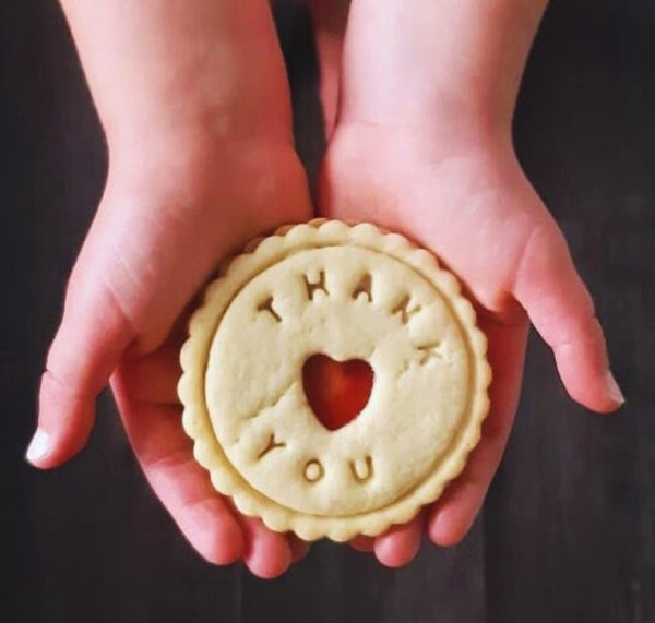 Child holding heart-shaped biscuit with "Thank You" written on it. Biscuit from The Biskery, personalised biscuit company.