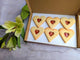 A box of heart-shaped BISCUITS with A JAM filling, next to a bouquet of flowers.