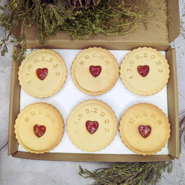Box containing six Jam wedding biscuits, with heart-shaped biscuits at the centre, arranged on a table, adorned with a yellow ribbon for the MR&MR couple 