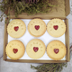 Box containing six Jam wedding biscuits, with heart-shaped biscuits at the centre, arranged on a table, adorned with a yellow ribbon for the MR&MR couple 